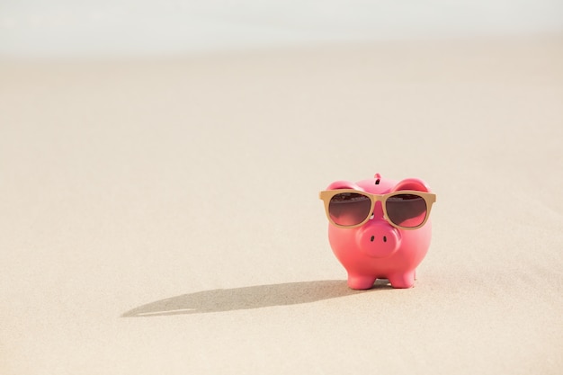 Free photo summer piggy bank with sunglasses on sand