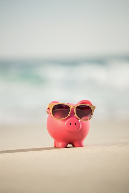 Summer piggy bank with sunglasses on sand