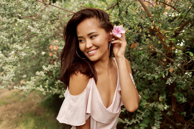 Free photo summer portrait of lovely asian woman with flower in hairs posing in the garden.