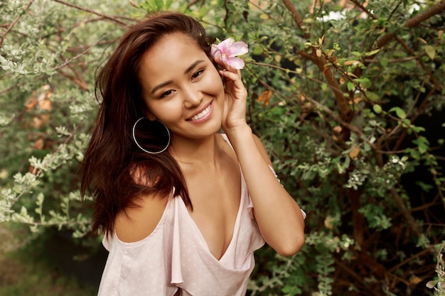 Summer portrait of lovely Asian woman with flower in hairs posing in the garden.