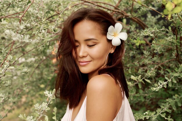 Summer portrait of lovely Asian woman with flower in hairs posing in the garden.