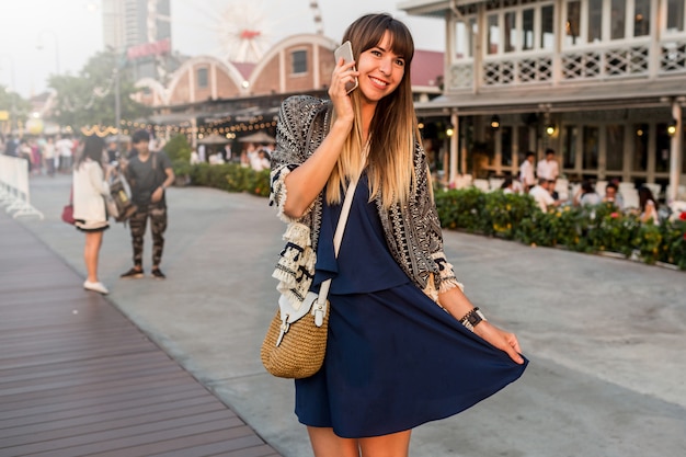 Summer  positive portrait of cheerful woman in stylish  outfit talking by mobile phone  and smiling on  Riverfront in Bangkok