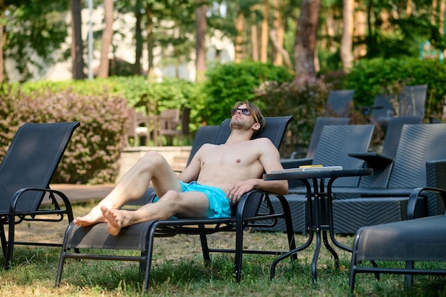 Free Photo sunbathing. young man in blue shorts sunbathing and looking relaxed