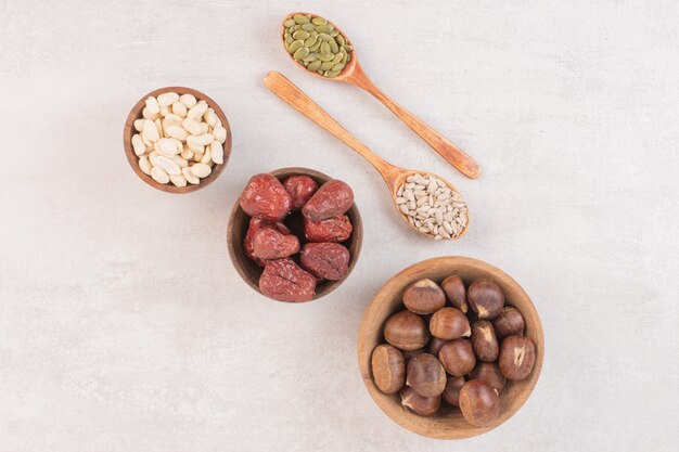 Sunflower and pumpkin seeds and bowls of nuts on white surface.