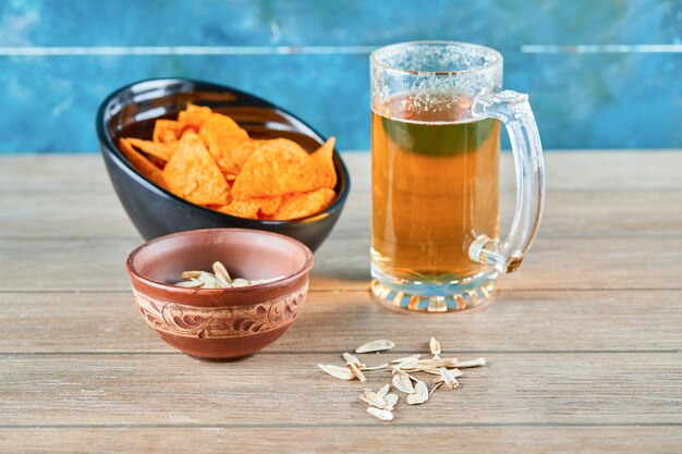 Sunflower seeds, a bowl of chips and a glass of beer on wooden table.