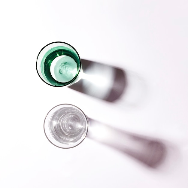 Sunlight falling on green and white glasses filled with water against white backdrop