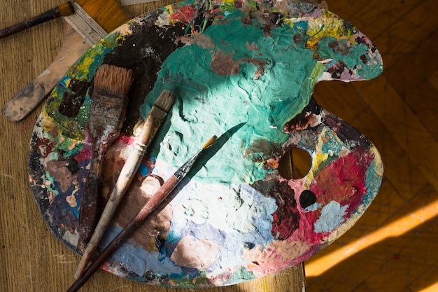 Free photo sunlight on messy palette and brush over wooden table