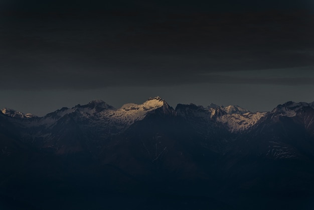 Sunlight shining a single mountain top at sunset with dark cloudy sky