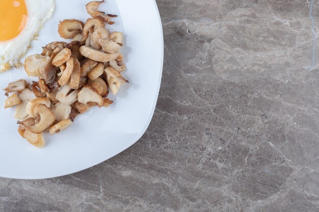 Sunny fried egg and mushrooms on white plate.