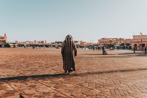 Sunny scenery of an Arabian male in stripped thawb walking in the big urban area