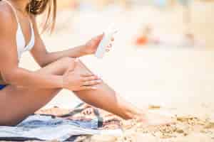 Free photo sunscreen suntan lotion in spray bottle. young woman in spraying tanning oil on her leg from bottle. lady is massaging sunscreen lotion while sunbathing at beach. female model during summer vacation.