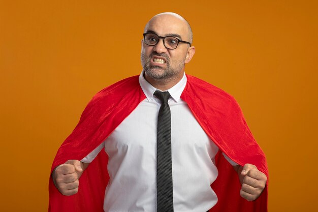 Super hero businessman in red cape and glasses clenching fists angry and frustrated 