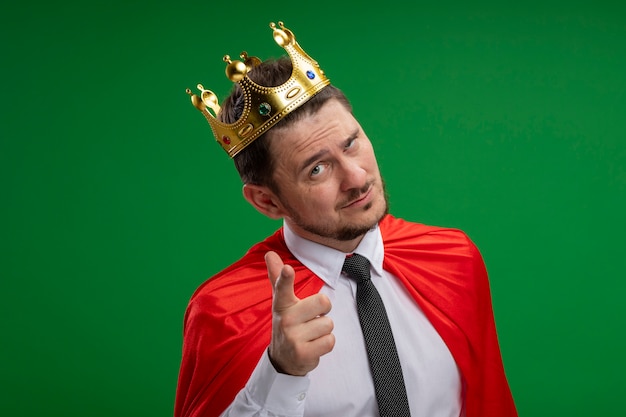 Free photo super hero businessman in red cape wearing crown looking at camera looking at camera smiling confident poiniting with index figner at camera standing over green background