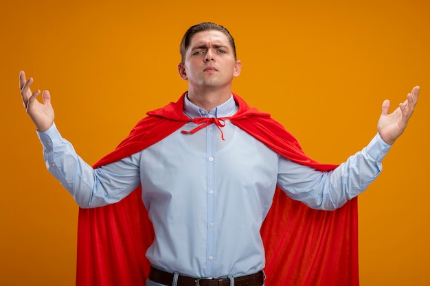 Super hero businessman in red cape  with raised arms being confident and proud standing over orange wall