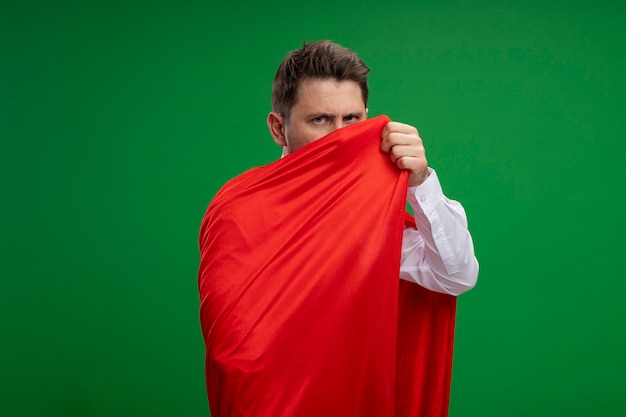 Super hero businessman wrapped with red cape looking at camera with serious face standing over green background