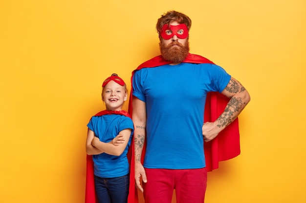 Free photo superhero family. powerful dad keeps one hand on waist, little child with arms crossed stands back