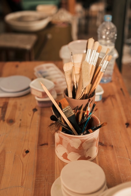 Free photo supplies with paint brushes and tools in handmade clay holder on wooden table