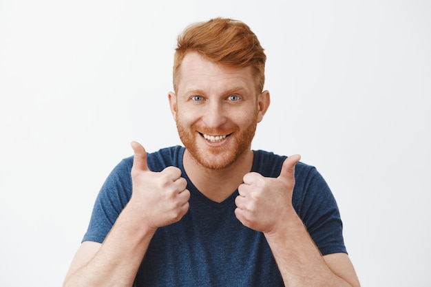 Free Photo supportive and attractive adult redhead male with bristle liking great plan raising hands, showing thumbs up, smiling joyfully