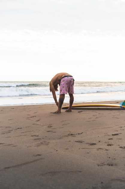 Free Photo a surfer man walks with a board on a sandy beach. handsome young man on the beach. water sports. healthy active lifestyle. surfing. summer vacation. extreme sport.