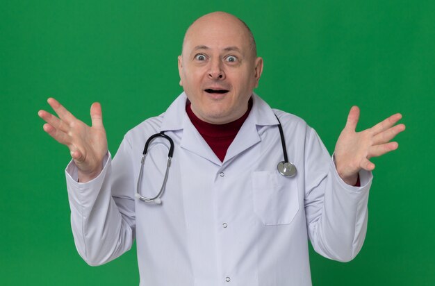 Surprised adult slavic man in doctor uniform with stethoscope keeping hands open and looking at front