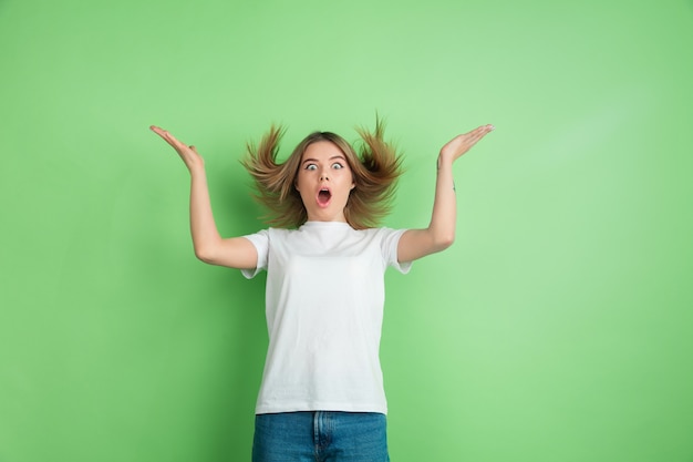 Surprised, astonished young woman isolated on green studio wall