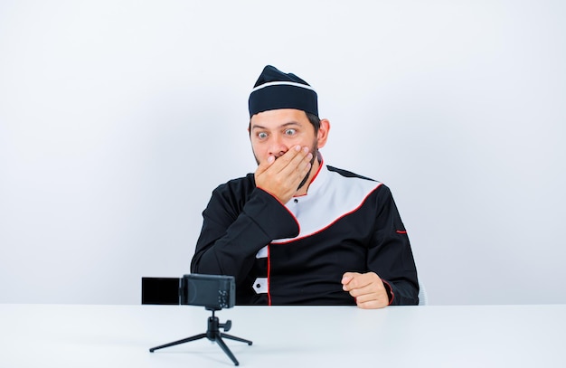 Surprised blogegr chef is looking at his mini camera by sitting on white background