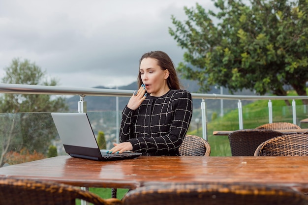 Surprised blogger girl is looking at her laptop screen by holding hand on mouth on nature view background