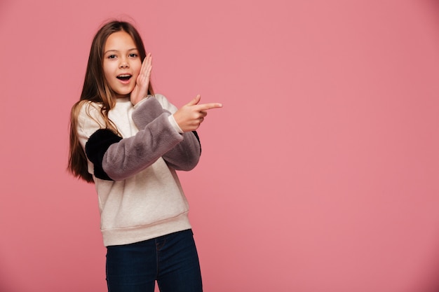 Surprised brunette girl pointing at copy space with opened mouth isolated