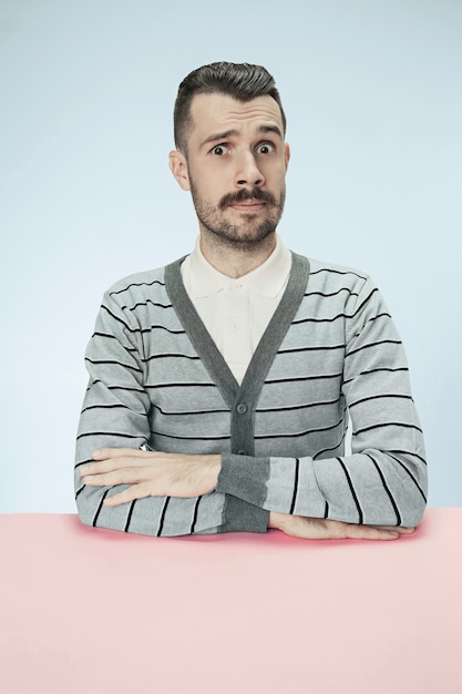 Surprised business man sitting at table on blue studio background. The portrait in minimalism style