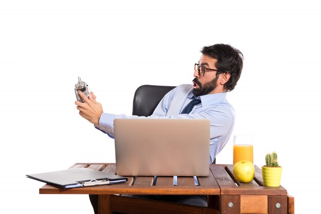 Free photo surprised businessman in his office holding a clock