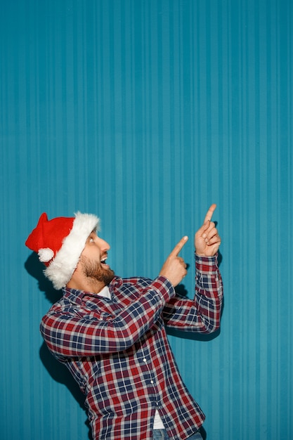 surprised christmas man wearing a santa hat showing anything on the blue studio background