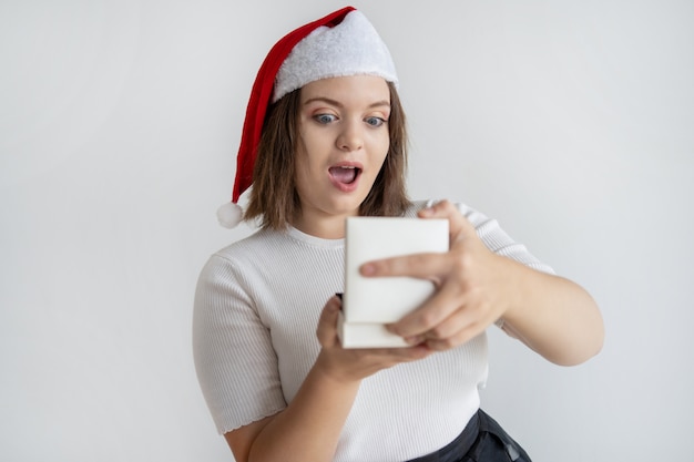 Surprised chubby girl in santa hat opening gift box