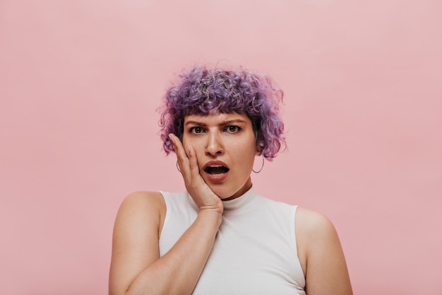 Free photo surprised curly woman in white top posing on. short-haired woman with round earrings on pink.