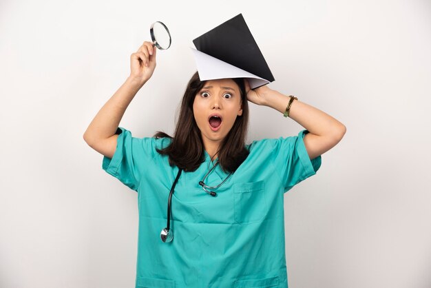 Surprised doctor holding magnifying glass and clipboard on white background. High quality photo