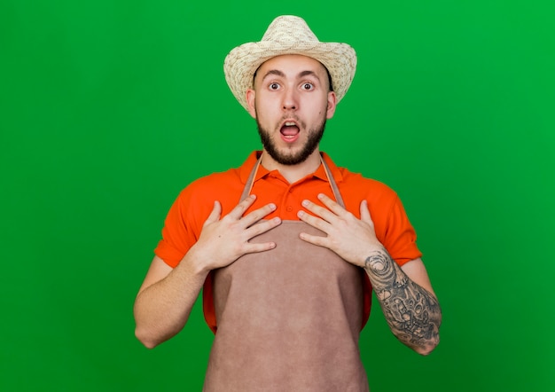 Surprised gardener man wearing gardening hat puts hands on chest