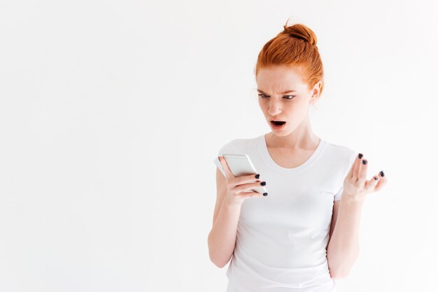 Surprised ginger woman in t-shirt looking at her smartphone