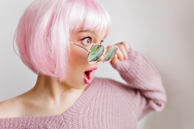 Free photo surprised girl with big eyes looking away during photoshoot. close-up photo of sensual young woman in pink peruke and sunglasses.