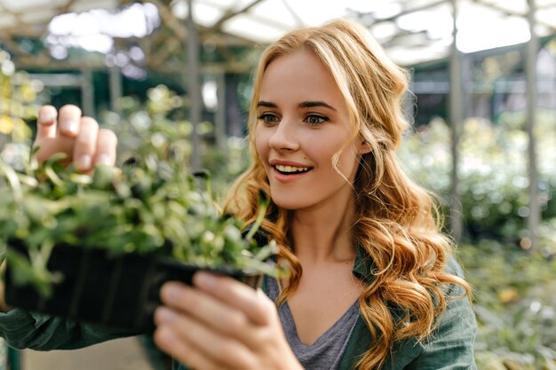 Surprised green-eyed lady looks at plant in amazement. Portrait of cute long-haired European model who loves botany.