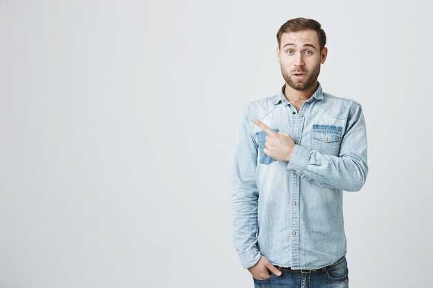 Surprised handsome bearded guy pointing finger left