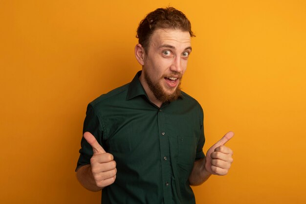 Surprised handsome blonde man thumbs up of two hands isolated on orange wall