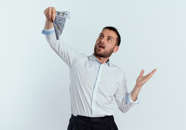 Surprised handsome man holds and looks at money isolated on white wall