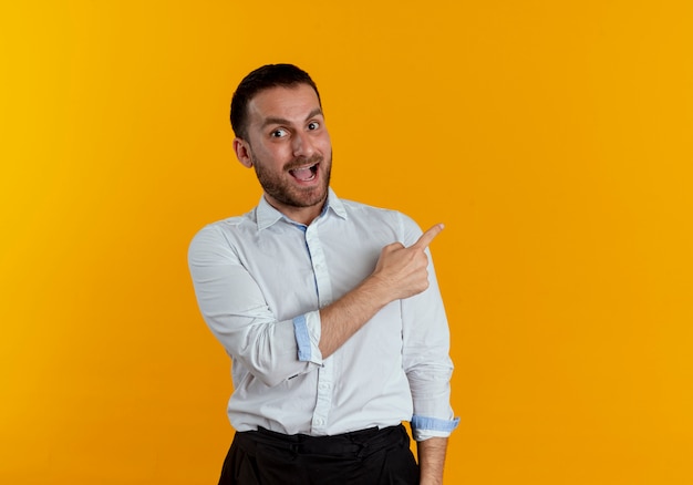 Surprised handsome man points at side looking isolated on orange wall