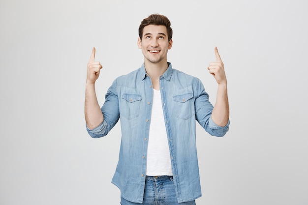 Surprised handsome man showing banner, pointing up