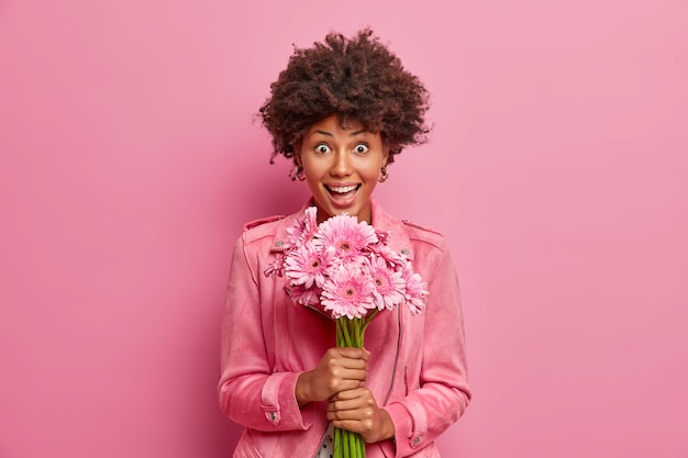 Surprised happy young woman with Afro hair holds beautiful gerbera flowers