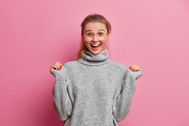 Surprised joyful young European woman raises hands and looks with excitement hears something excellent