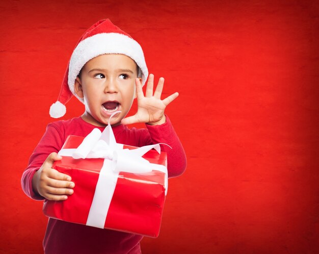 Surprised little boy with santa hat and a gift