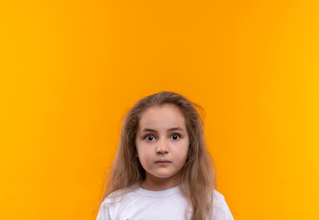 Surprised little school girl wearing white t-shirt on isolated orange background