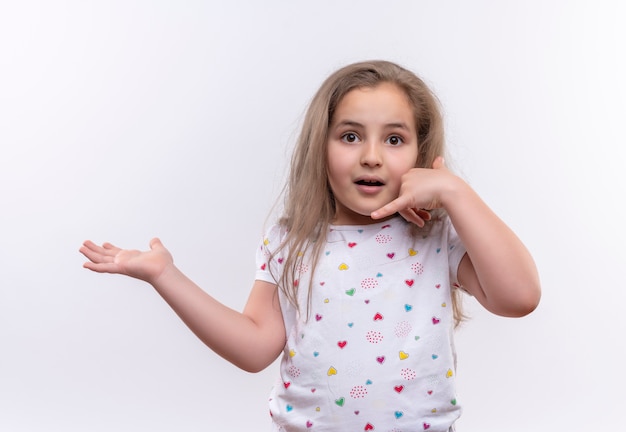 Surprised little school girl wearing white t-shirt showing call gesture on isolated white background