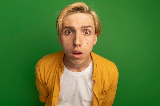 Free photo surprised looking straight ahead young blonde guy wearing yellow t-shirt isolated on green