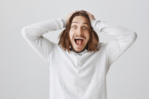 Free photo surprised lucky guy smiling and laughing from happiness, holding hands on head